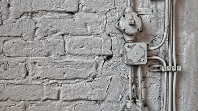 An electrician marking a cable route on bare brick beside an open loft hatch